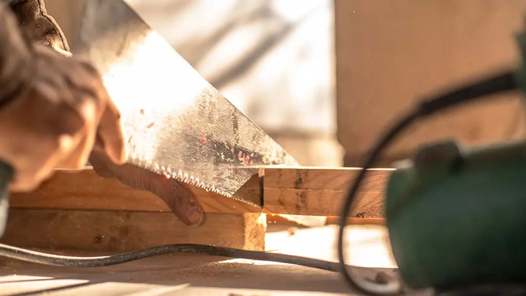close up view of a carpenter using a handsaw to cut a piece of wood board